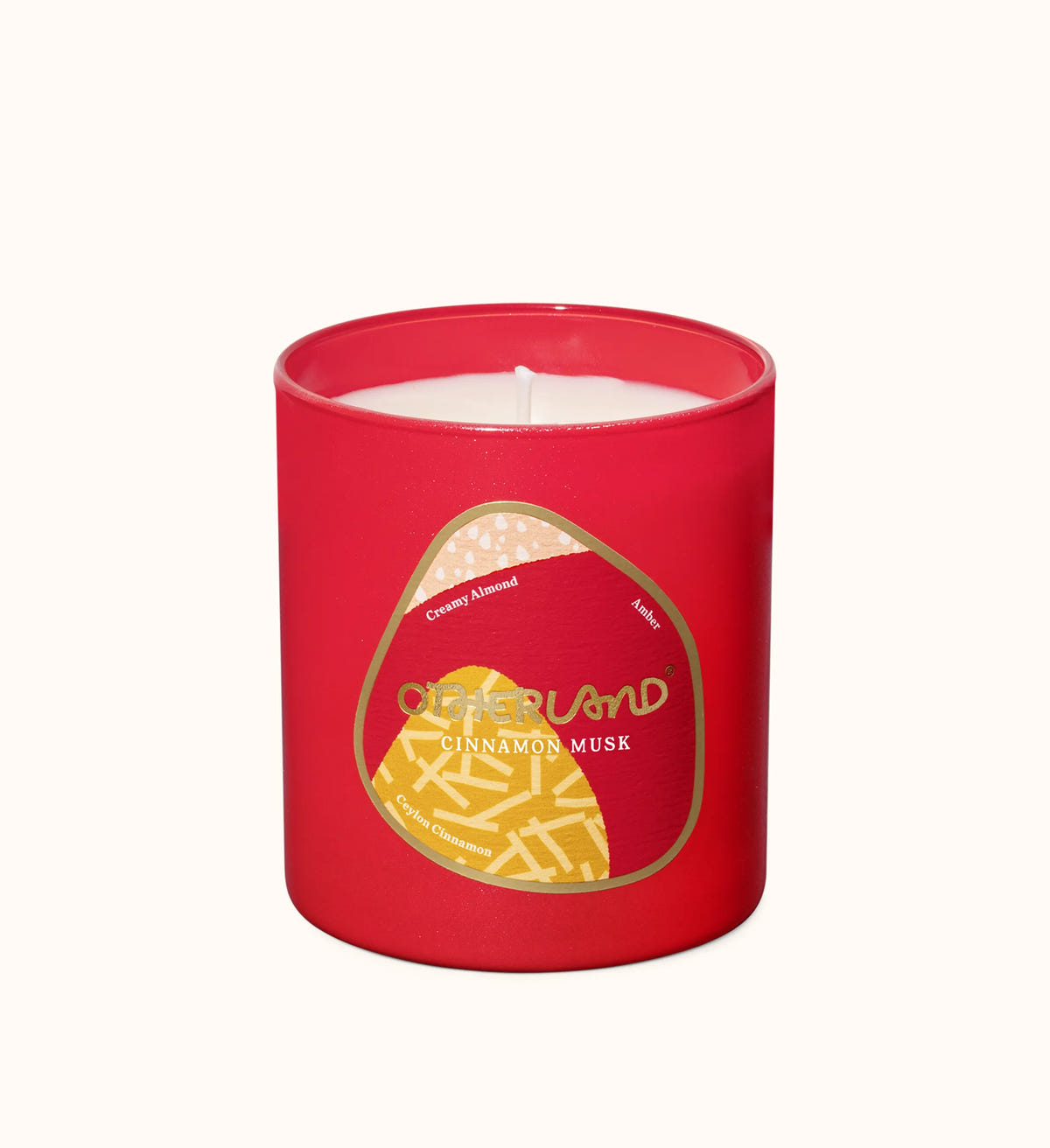 A red glass jar candle with white wax inside, featuring a gold and beige label that reads 'OCEANLAND CINNAMON MUSK' on a plain off-white background.