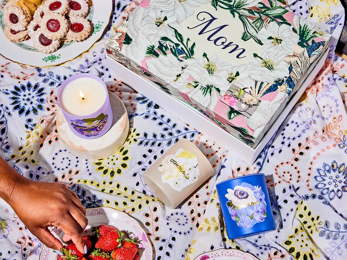 Gift box with floral design and 'Mom' text on a colorful tablecloth with candles and cookies.