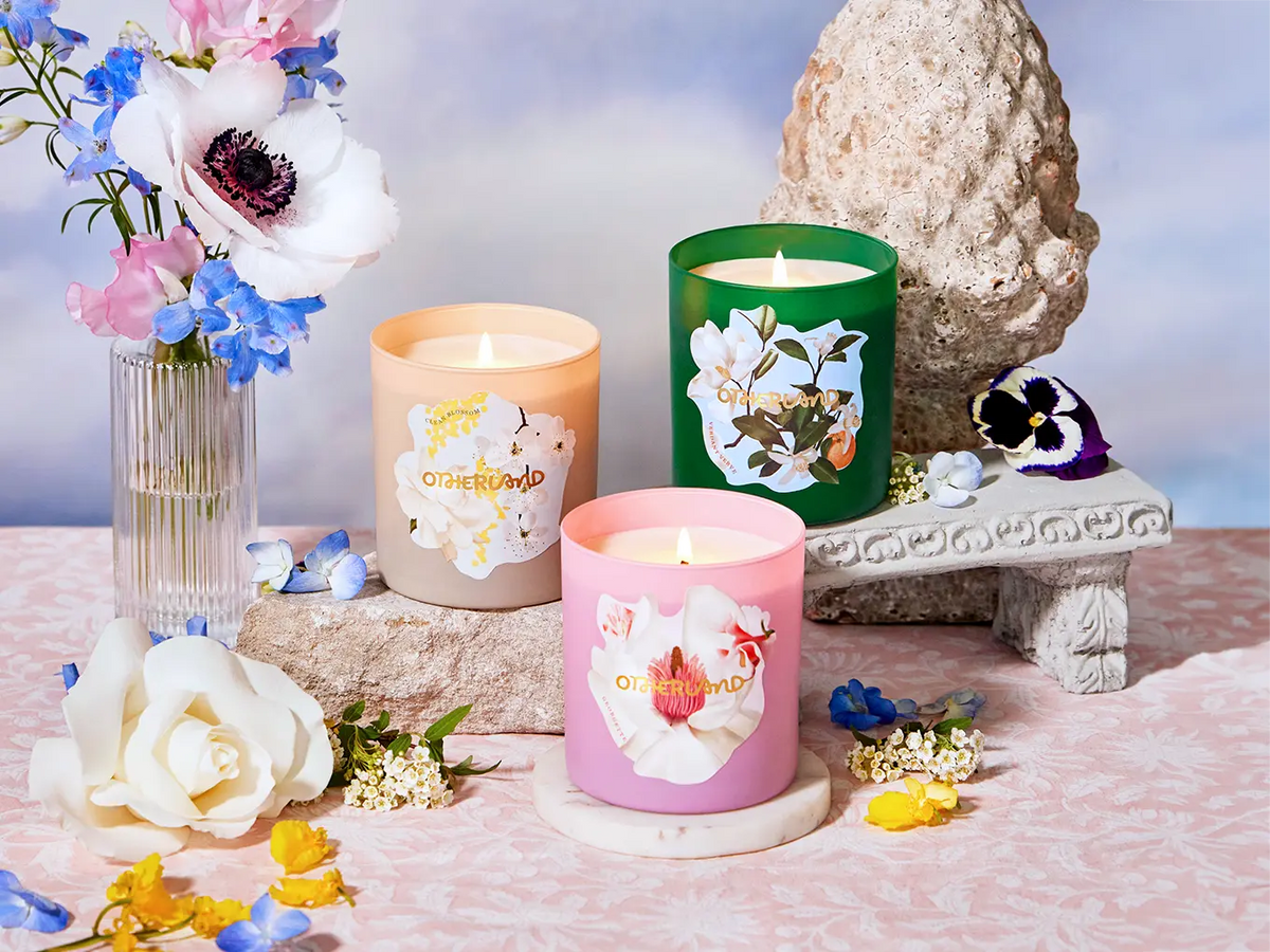 Three scented candles with floral designs on a decorative table with flowers and a stone sculpture.