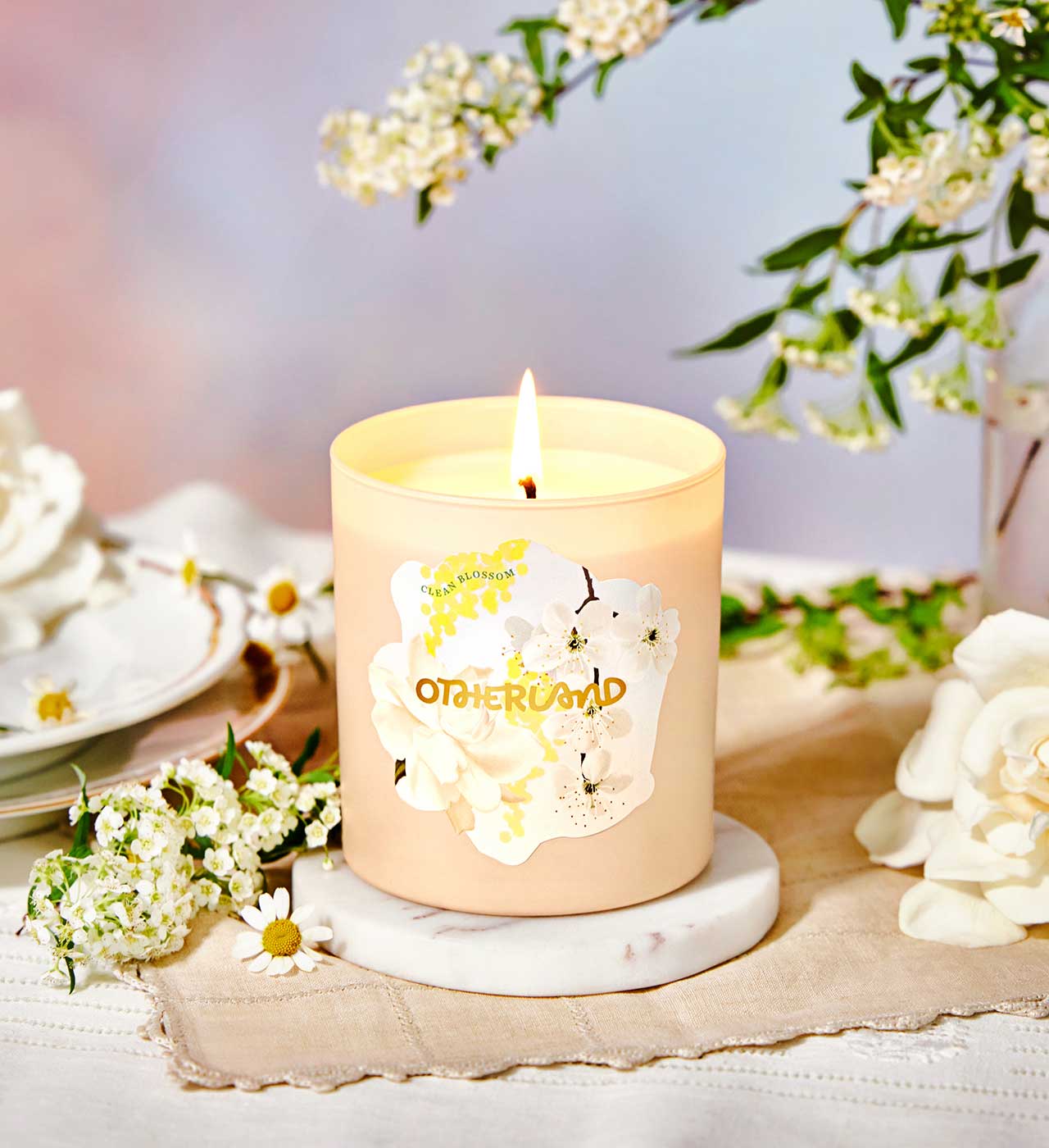 Candle with a floral design on a marble coaster surrounded by flowers and tea cups.