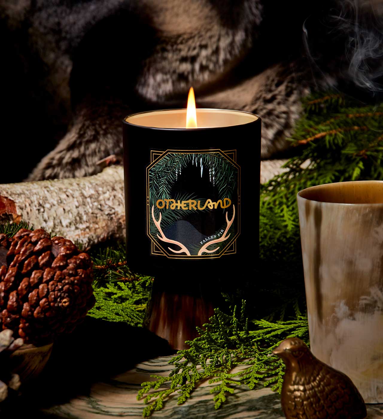 Candle with 'Otherland' branding in a natural setting with greenery and a log.