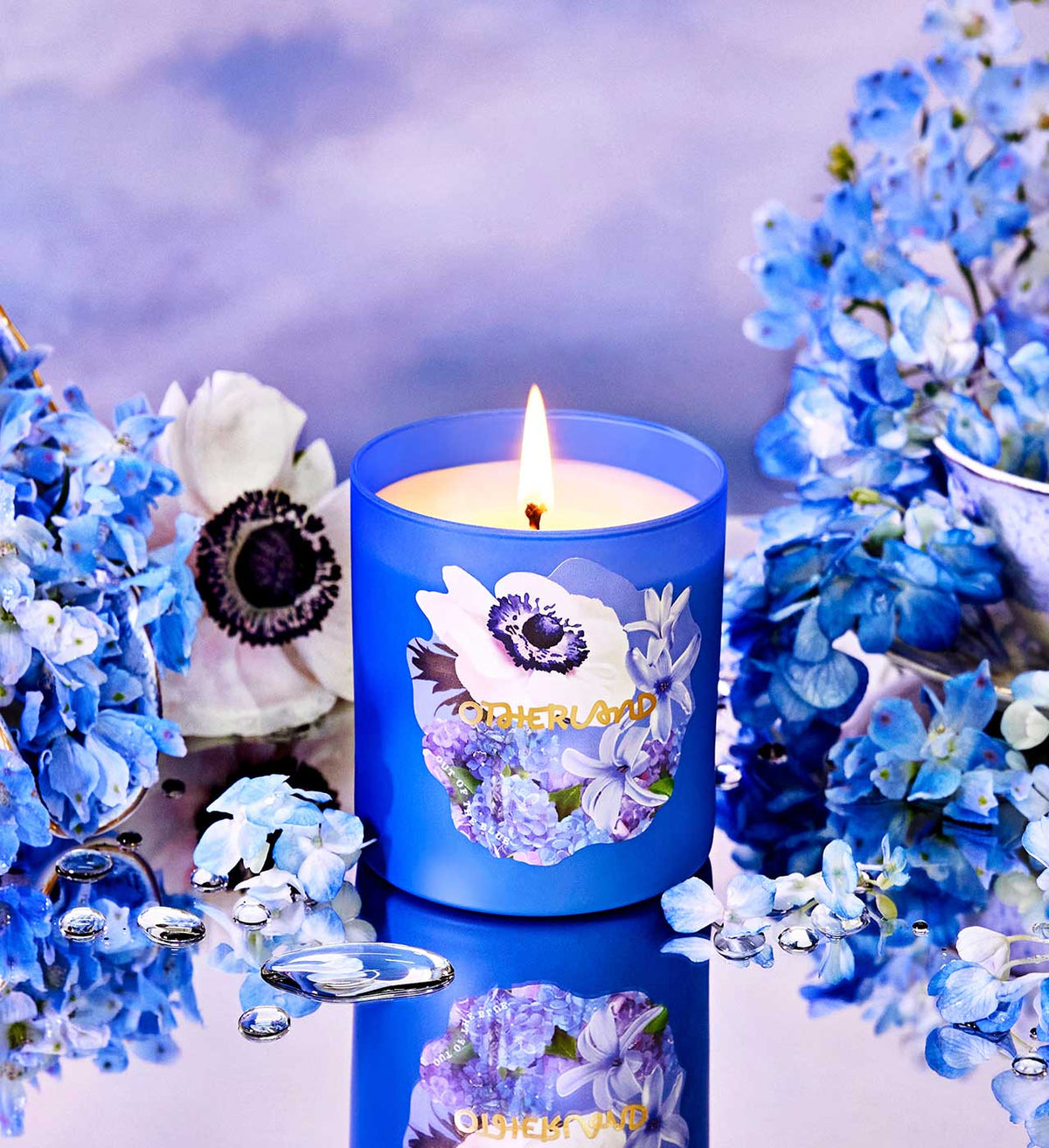 Blue candle with floral design surrounded by blue flowers on a reflective surface