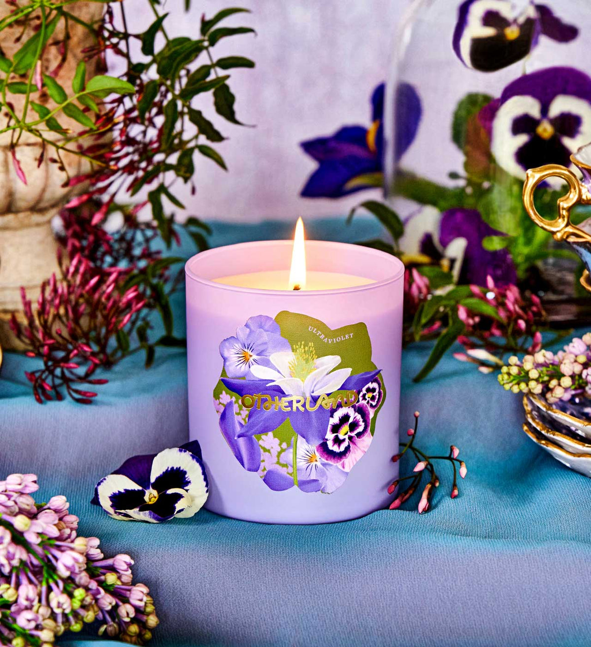 Purple candle with floral design on a table with flowers and plants